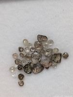 Close-up image of multiple small raw natural diamonds scattered on a white foam background, showing varying color, size, and clarity.