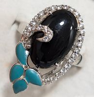 Close-up front view of sterling silver ring featuring oval black onyx center stone surrounded by clear cubic zirconia and turquoise leaf-shaped enamel accents.