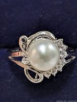 Top view showing central large white pearl surrounded by clear cubic zirconia stones with an elegant swirl design silver band.