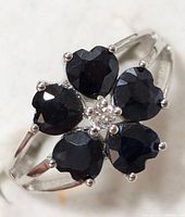 Close-up image showing sterling silver ring with five heart-shaped blue sapphires arranged like flower petals and a small clear stone in the center.