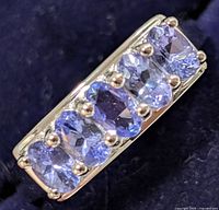 Close-up of the top of the sterling silver ring showcasing five oval-cut tanzanite gemstones set in a row with bead prongs.
