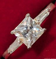 Close-up view of the silver ring showing the princess-cut central CZ and tapered baguette CZ side stones on a polished silver band.