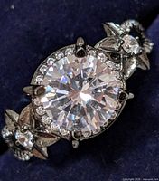 Close-up of sterling silver ring with a large round central cubic zirconia stone, surrounded by smaller stones and floral design on band.