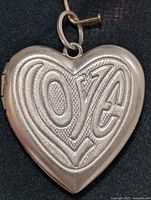 Front view of heart-shaped silver locket pendant with embossed decorative pattern.