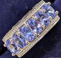 Close-up photo of the silver ring showing seven oval tanzanite stones and detailed bead accents on the band.