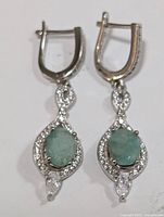 Front view of a pair of silver drop earrings with oval emerald stones surrounded by cubic zirconia and a marquise CZ stone at the bottom
