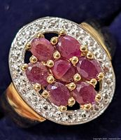 Close-up top view of ring showing seven oval-cut rubies and surrounding accent stones