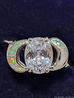 Close-up front view of sterling silver ring highlighting cushion-cut clear cubic zirconia center stone and opal crescent-shaped inlays on sides