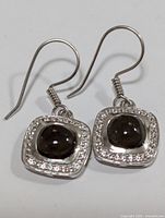 Pair of sterling silver drop earrings with cushion-shaped smokey quartz stones surrounded by clear accent stones, shown front view with hooks visible.