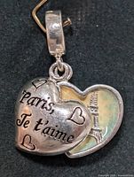 Heart-shaped charm with 'Paris, Je t'aime' engraving and inner side showing Eiffel Tower image.