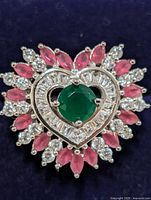 Close-up of ring's face showing green onyx center surrounded by heart-shaped cubic zirconia and ruby stones.