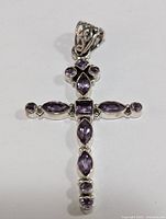 Top-down view of silver cross pendant with amethyst stones, displaying the shape, stone cuts, and filigree bail details