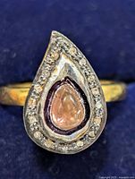 Front view of a pear-shaped silver ring with pink tourmaline center and surrounding diamonds on a gold-tone band.