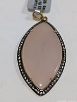 Top view of a marquise-shaped rose quartz pendant set in silver with clear stone accents around bezel and gold-tone bail.