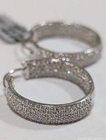 Close-up of the pair of silver hoop earrings encrusted with small cubic zirconia stones on the outer surface.