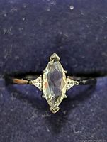 Front view of silver ring with marquise-cut clear central gemstone and side accents on a dark fabric background.