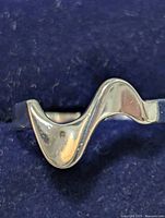Close-up photo of silver ring against dark fabric background showing the wave design on the ring's top surface.