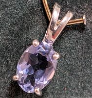 Close-up image of silver pendant showing oval faceted tanzanite gemstone held by four prongs on a silver bail.