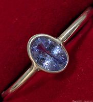 Close-up image of the silver ring showing the oval tanzanite gemstone and silver band on a red background