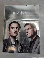 Front cover of Nip/Tuck The Complete Series DVD box set showing two men on glossy reflective packaging.