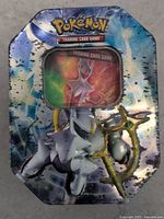 Pokemon Trading Card Game metal tin with Arceus design on the lid, showing some wear and minor dents.