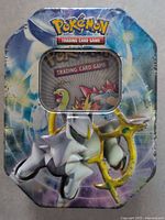 Metal tin with Arceus artwork and window showing Pokemon Trading Card Game logo