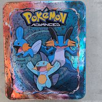 Photo of the Pokemon Advanced metal storage tin with Mudkip, Marshtomp, Swampert artwork on lid, showing holographic and colorful finish.