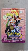 Front of the Pokemon 3 trading card game metal tin featuring Pokemon characters and artwork with pink background.