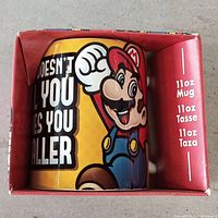Front side view of the boxed mug showing the Mario character and size details (11oz) on the packaging.