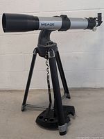 Side view of the Meade DS-208AT telescope on tripod showing optical tube, tripod legs, and attached hand control.