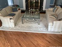 Wide view of off-white wool area rug under glass-top coffee table and flanked by sofas on hardwood floor