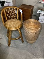 Photo of rattan style swivel bar height chair with wicker seat and round wicker laundry basket with lid next to chair.