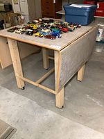 View of craft table showing one drop leaf extended and caster wheels underneath