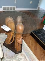 Side view of the carved wood base shaped as three cats holding a glass oval top.