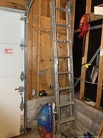 16 ft aluminum extension ladder leaned against wall near garage door, showing full length and environment