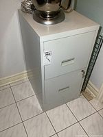 White 2-drawer metal file cabinet with keys, showing side and drawers with handles and lock.