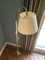 Full view of the floor lamp turned on, showing adjustable arm, pleated shade, and brass base.