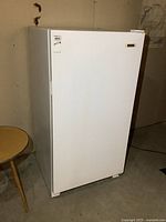 Front left angle view of the upright freezer showing overall unit with white finish and closed door.