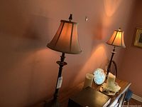 Photo of both table lamps on furniture against peach colored wall showing one lamp fully lit and the other partially visible.