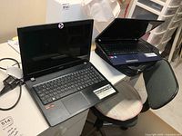 Two Acer laptops positioned on chairs and desk. Both have 15.6-inch screens and black keyboards. One laptop has visible AMD A9 and Radeon stickers.