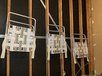 Three vintage aluminum lawn chairs with white and rainbow webbing folded and hanging on wall-mounted hooks