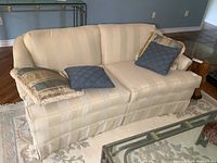 Front view of the light beige upholstered loveseat with cushions on a patterned rug showing sofa shape and cushion details.