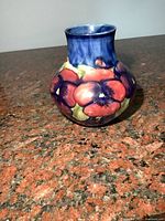 Front view of the Moorcroft vase showing red and purple pansy flowers with green leaves on blue background.