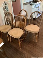 Set of six solid oak dining chairs, arranged in a group on a dark wood floor showing chairs with beige cushioned seats.