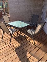 Full set of patio table and four chairs on wooden deck under sunlight.