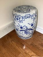 Porcelain barrel-shaped garden stool with blue floral and geometric pattern sitting on wood floor near baseboard.