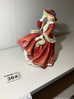 Oblique side view of Royal Doulton Top o the Hill figurine in red dress with hat.