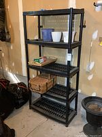 Full view of black resin five-tier plastic shelf standing against a wall with some items on it for scale.