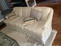Angle view of cream and beige vertically striped sofa with three cushions, placed on a floral rug.