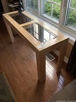 Full side view of the wooden sofa table by the window showing two inset beveled glass panels.